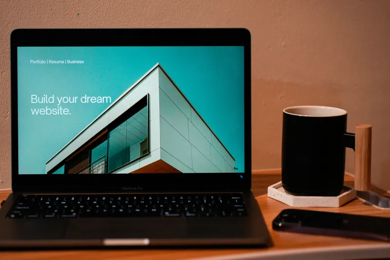 A laptop on a desk with a website on screen, next to a mug